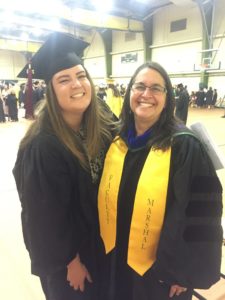 A student and faculty member celebrate graduation in graduation caps and gowns.