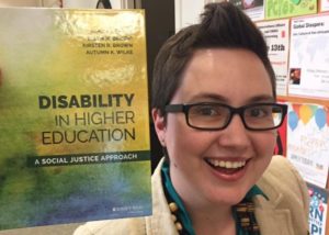 Autumn Wilke posing with her book, "Disability in Higher Education"