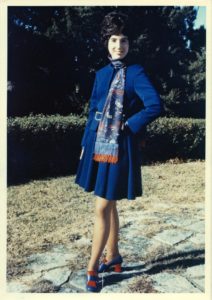 A young woman poses in a stylish blue dress she designed.