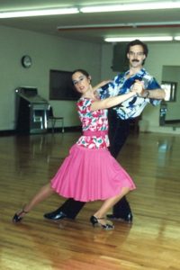 A woman lunges dramatically with her ballroom partner in a dance studio.