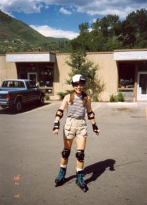 A woman rollerblades in a parking lot with a mountain backdrop.
