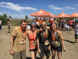 Four adults covered in mud embrace after an all-terrain race.