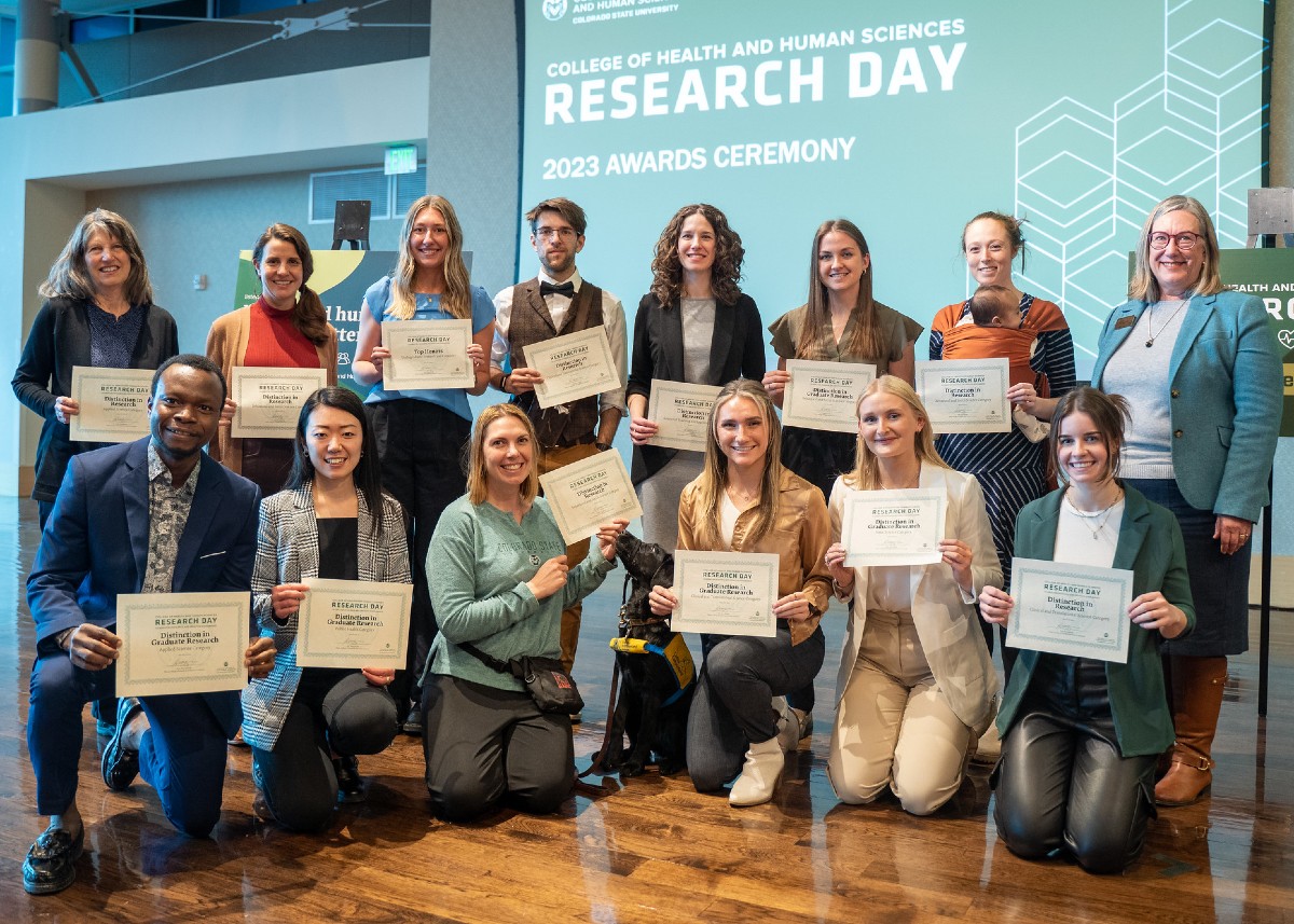 A group of 13 award winners holding certificates with a women standing next to them.