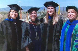 Four women wearing academic regalia smile in the Colorado sunshine with mountains in the distance