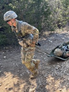 A soldier in camouflage gear hauls another soldier in a ground stretcher.