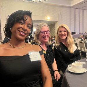 A Black woman and two white women in cocktail attire take a selfie at a banquet