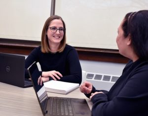 A professor and student sit at a table with open laptops