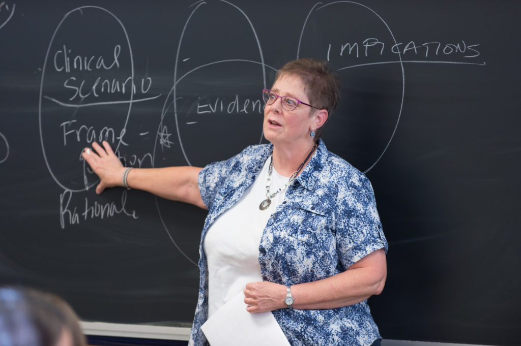 Karen Atler motioning toward a chalkboard while teaching in front of a class