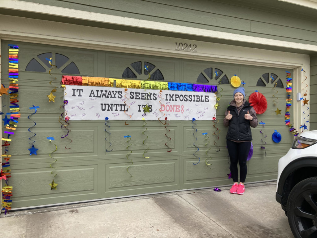 Ashley Montijo standing in front a banner and streamers hanging on a garage celebrating her defeating cancer