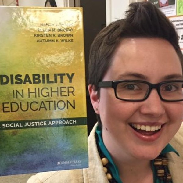 Someone holding a book titled 'Disability in Higher Education'
