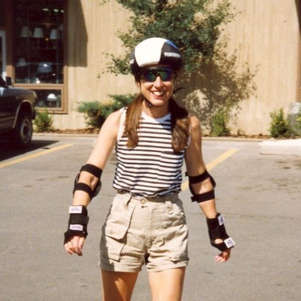 A person roller-skating wearing a helmet, elbow pads, wrist guards, and sunglasses