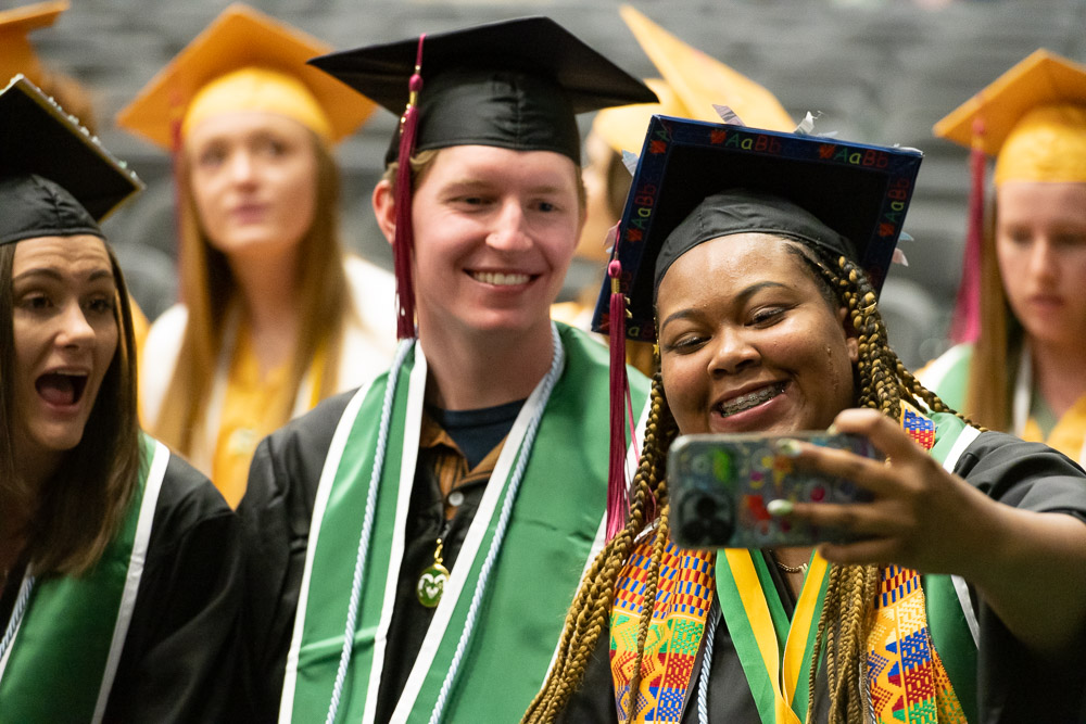 A diverse group of students in caps and gowns pose for a selfie