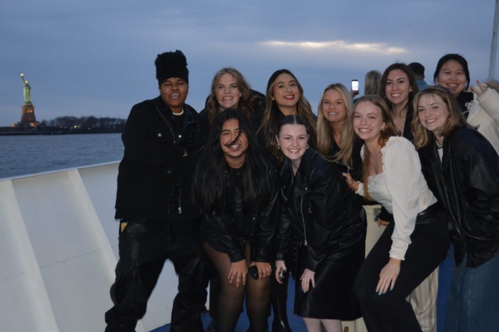 ten students from the study tour pose for a photo on a night time cruise with the statue of liberty in the background