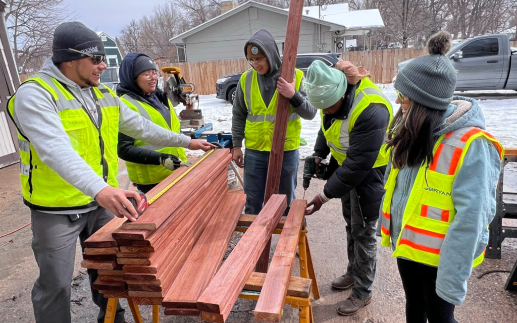 5 students, males and females, in reflective vests, working with lumber