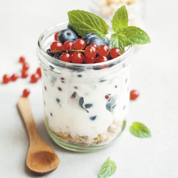 A parfait with berries, mint, and a wooden spoon in a glass container
