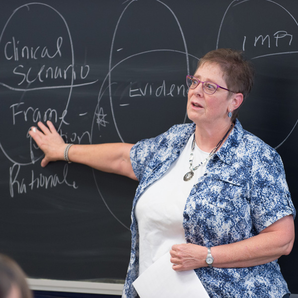 Karen Atler motioning toward a chalkboard while teaching