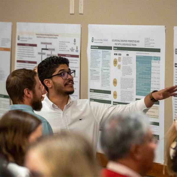 A student pointing to his research poster while talking to an interested person