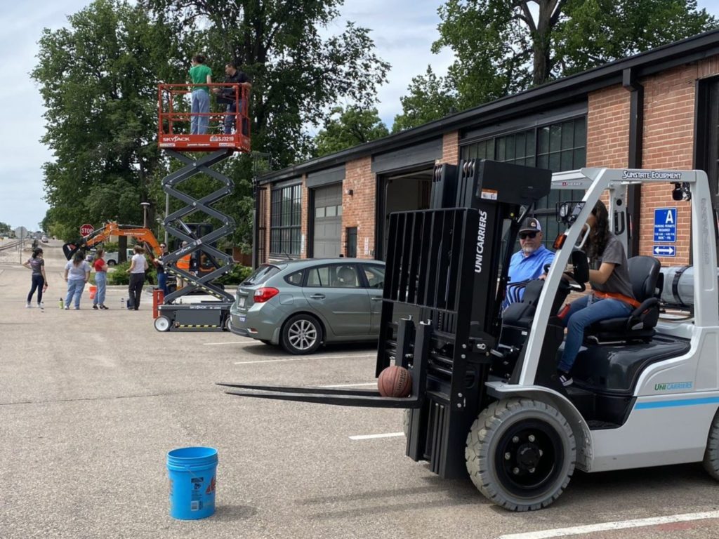 A fork lift, scissor lift, and a mini-excavator with students learning to operate the equipment