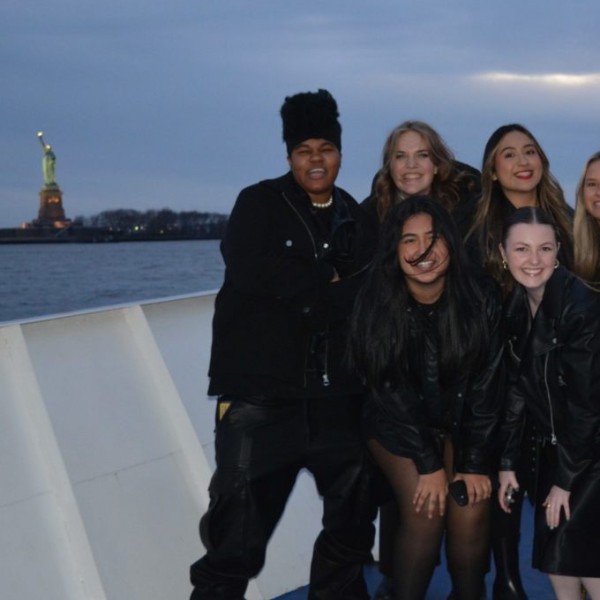 Students posing on a ferry in NYC with the statue of liberty in the background