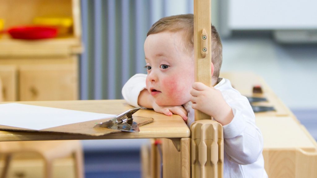 Child with rosey cheeks rests his head on a table that has a clipboard on it.