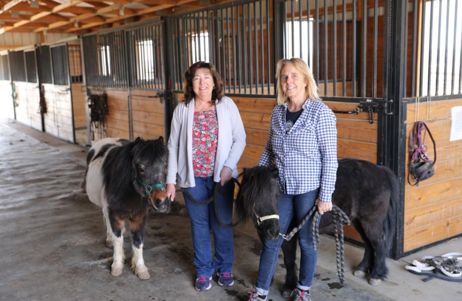 Kendy Brosh Smith and Mary Inkret Slouka posing with min horses in a stable