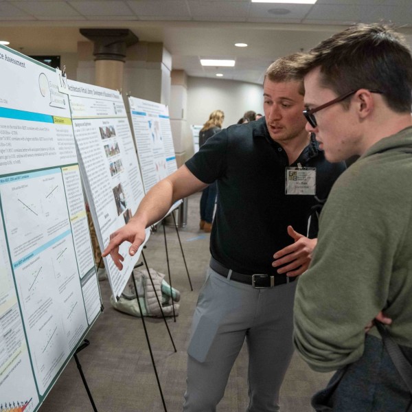 Matthew Scarsbrook talking to a person while motioning to his research poster