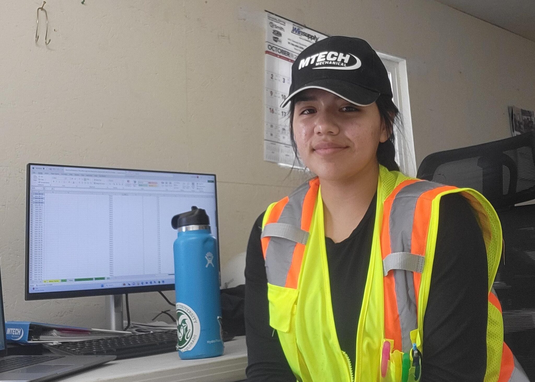 Latina student wearing a safety vest and MTech cap in a construction site office