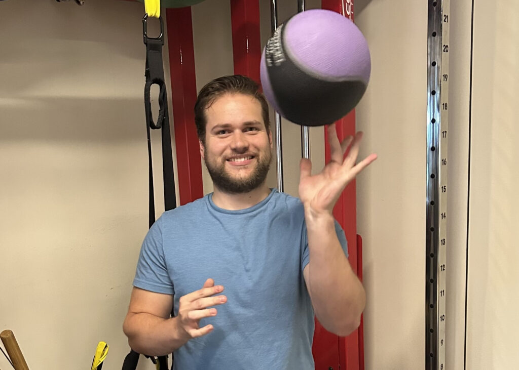 Danny Rice spinning a ball on his left index finger, in front of exercise equipment.