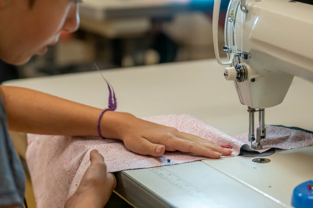 A student pushes a piece of fabric into a sewing machine needle