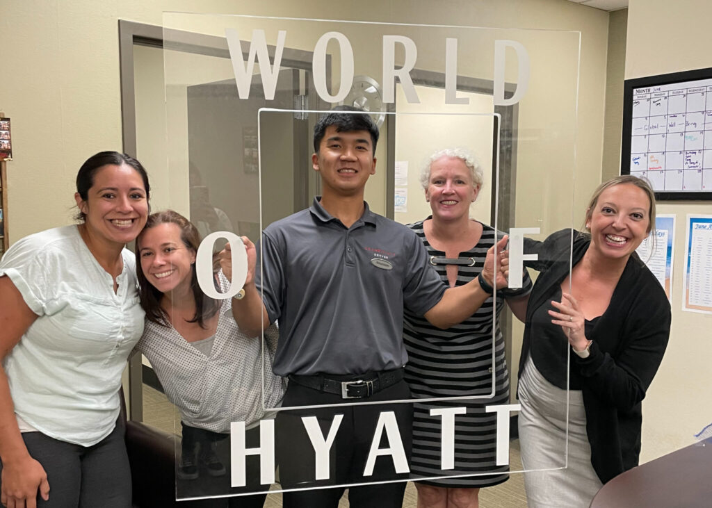 Ilkhomiddin, holding a 'World of Hyatt' display board, smiling with four other staff members