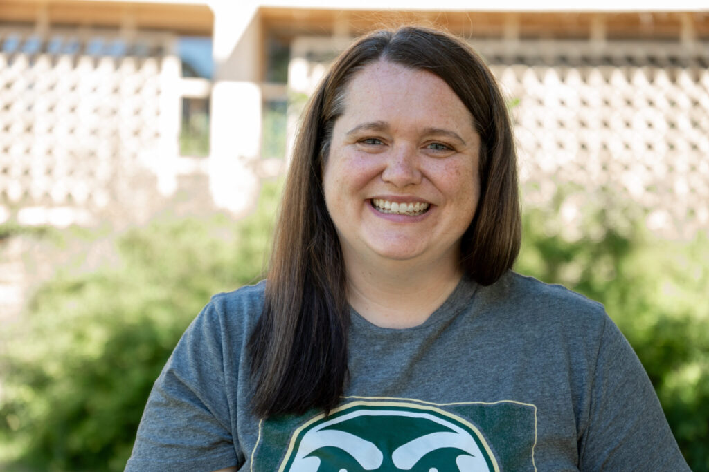 Andrea smiles for a photo in front of the Education building on Colorado State University's campus wearing a gray CSU shirt