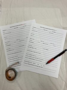 Two paper forms laid on a table with a tape measure and pen laying on top