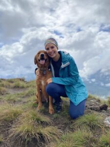 Guy and her golden retriever pose for a photo during a hike