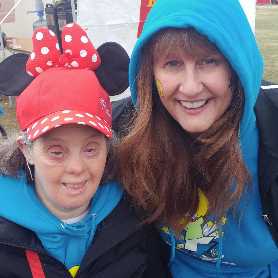 Michele and Carrie smile wearing blue sweatshirts and Carrie has a red Minnie Mouse hat
