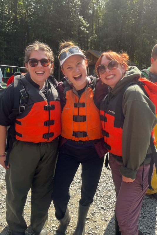 Three people smile wearing orange life jackets