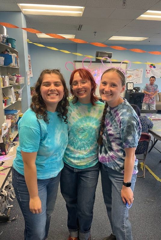 Three individuals pose in classroom wearing tie-dye shirts