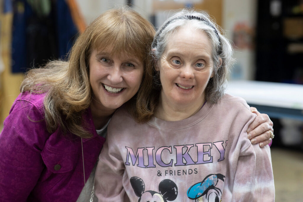 Michelle and Carrie smile with Carrie wearing a pink Mickey and Friends sweatshirt