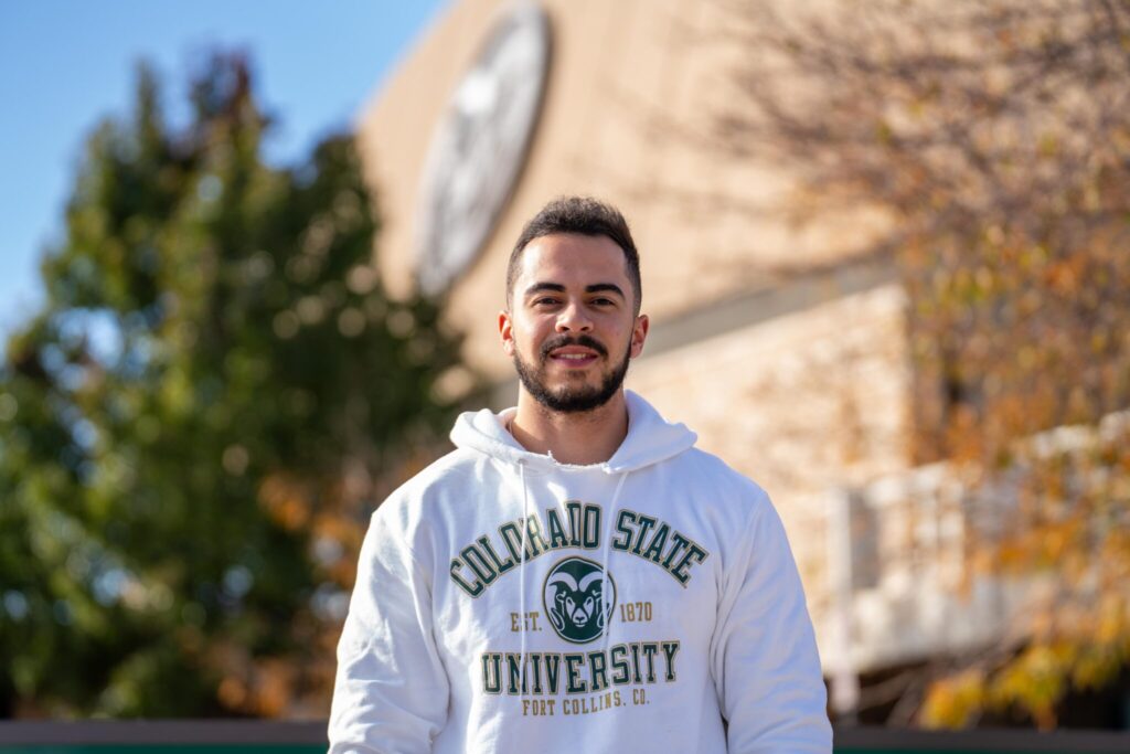 Chris smiles wearing a white CSU hoodie outside of Moby Arena.