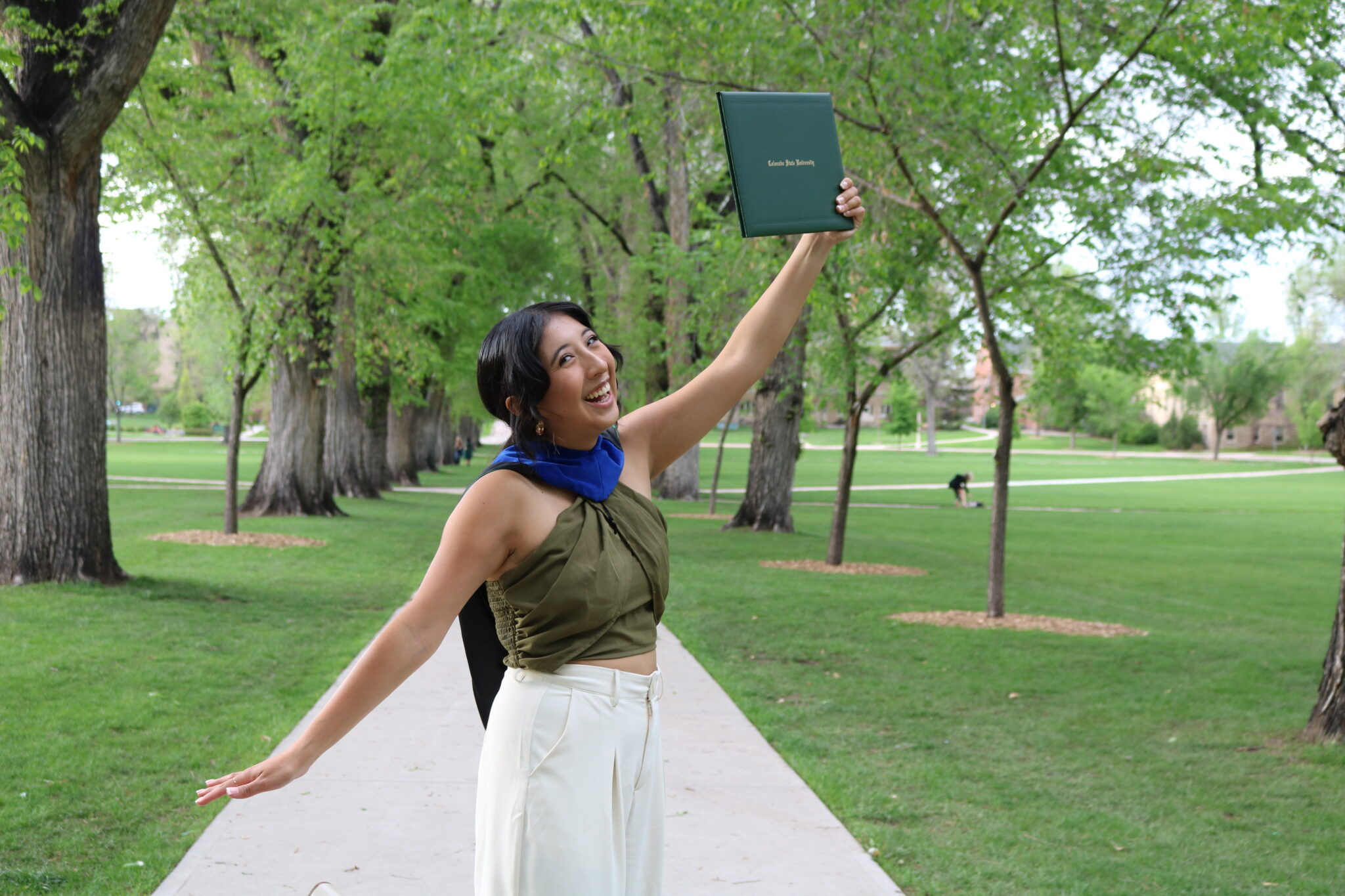 Servan-Alvarez holds up her diploma in the oval wearing dressier attire of a green shirt and cream pants.