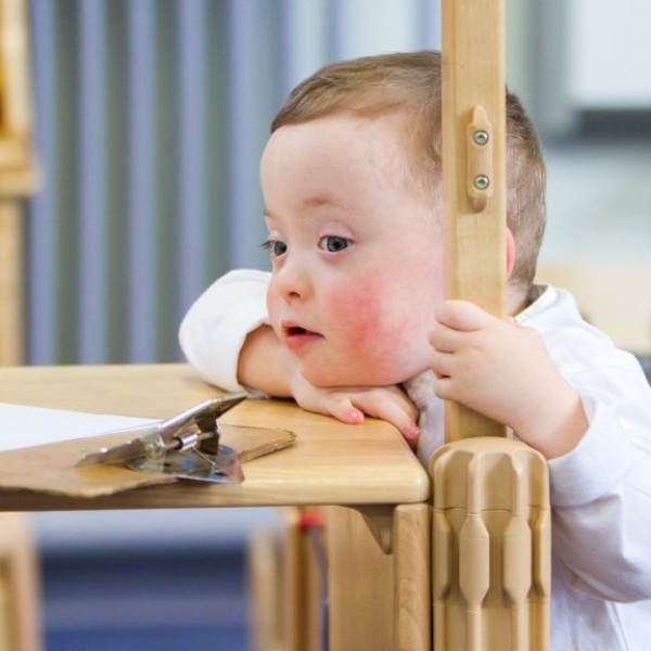 A child with Down Syndrome resting their chin on a wooden table