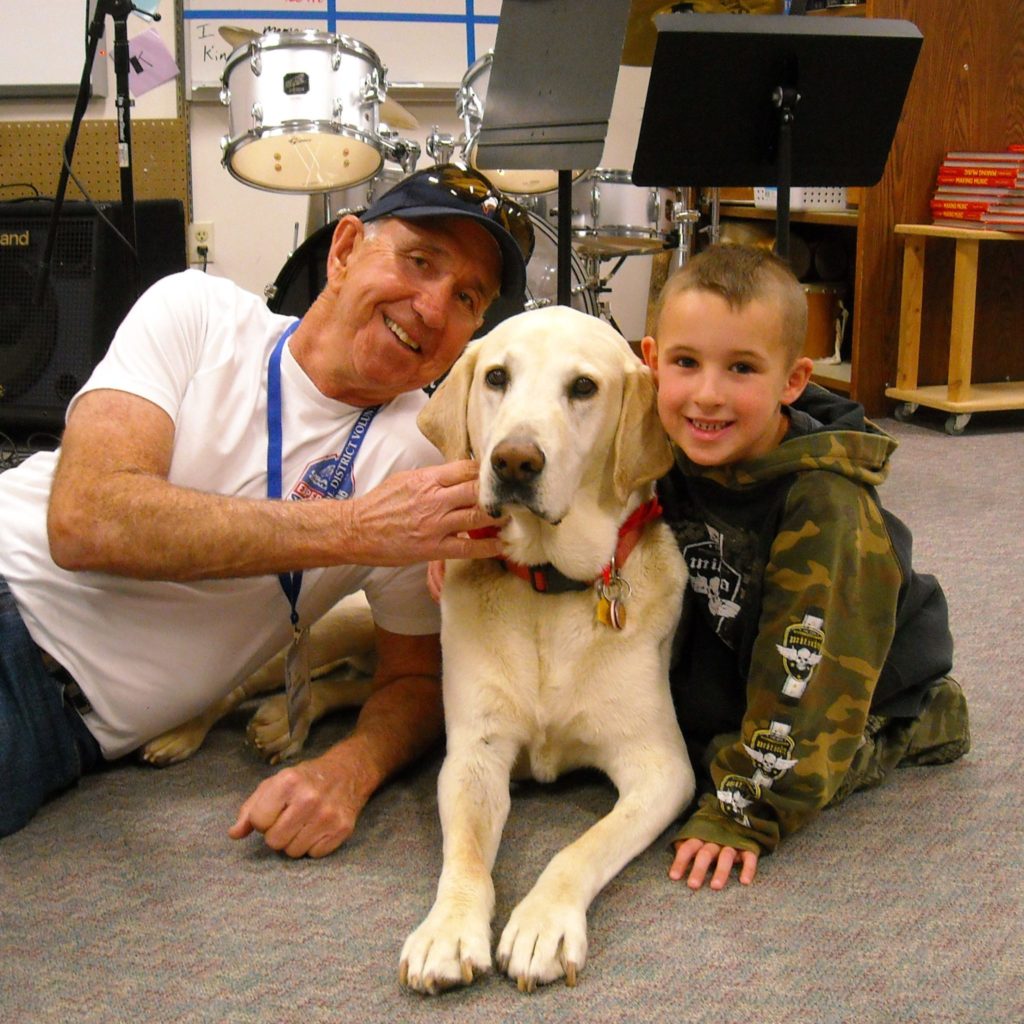 A person and a child sitting on the floor with a yellow Labrador dog