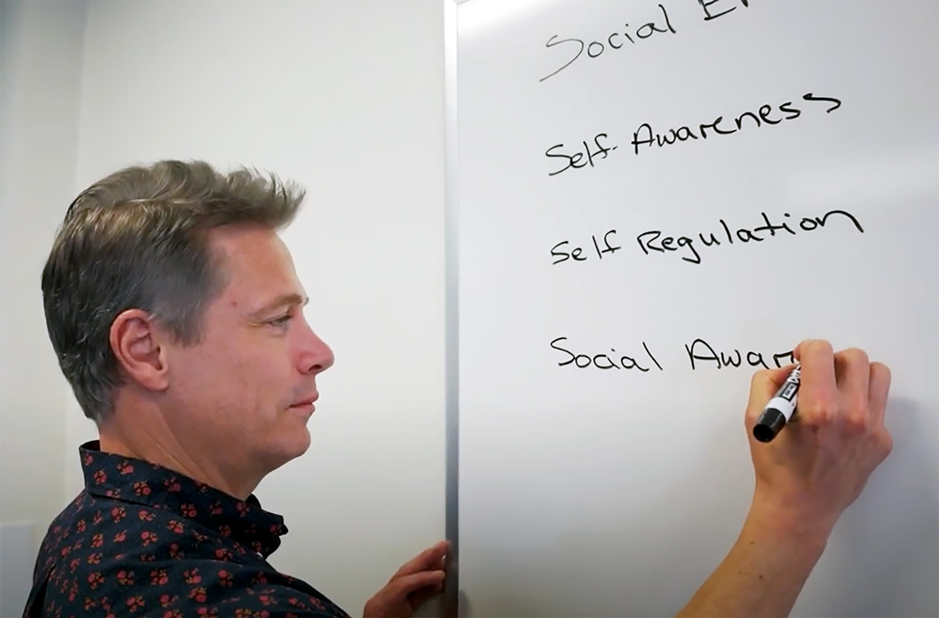 A person writing the words "self awareness", "self regulation", and "social awareness" on a whiteboard