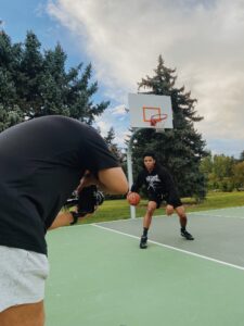 Man with camera filming another man in a black hoodie playing basketball