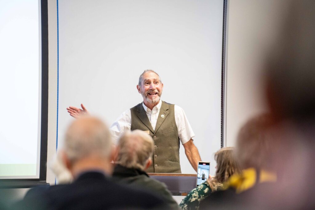 A bearded man in a vest speaks to a crowd