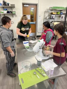 Hartman shows 3 culinary students how to use a citrus zester while in an industrial kitchen.