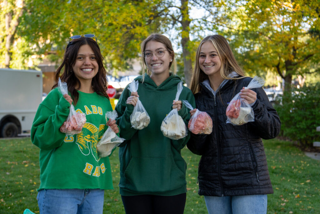 Three female gerontology students hold up bagged produce.