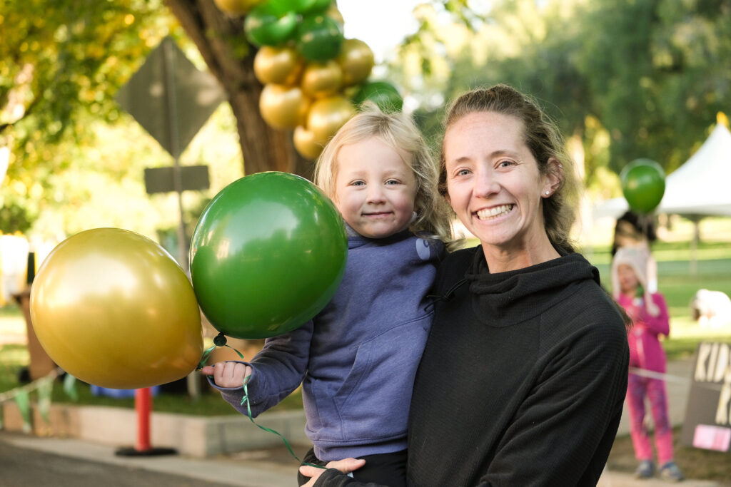 Mom and daughter smile while holding green and gold balloons