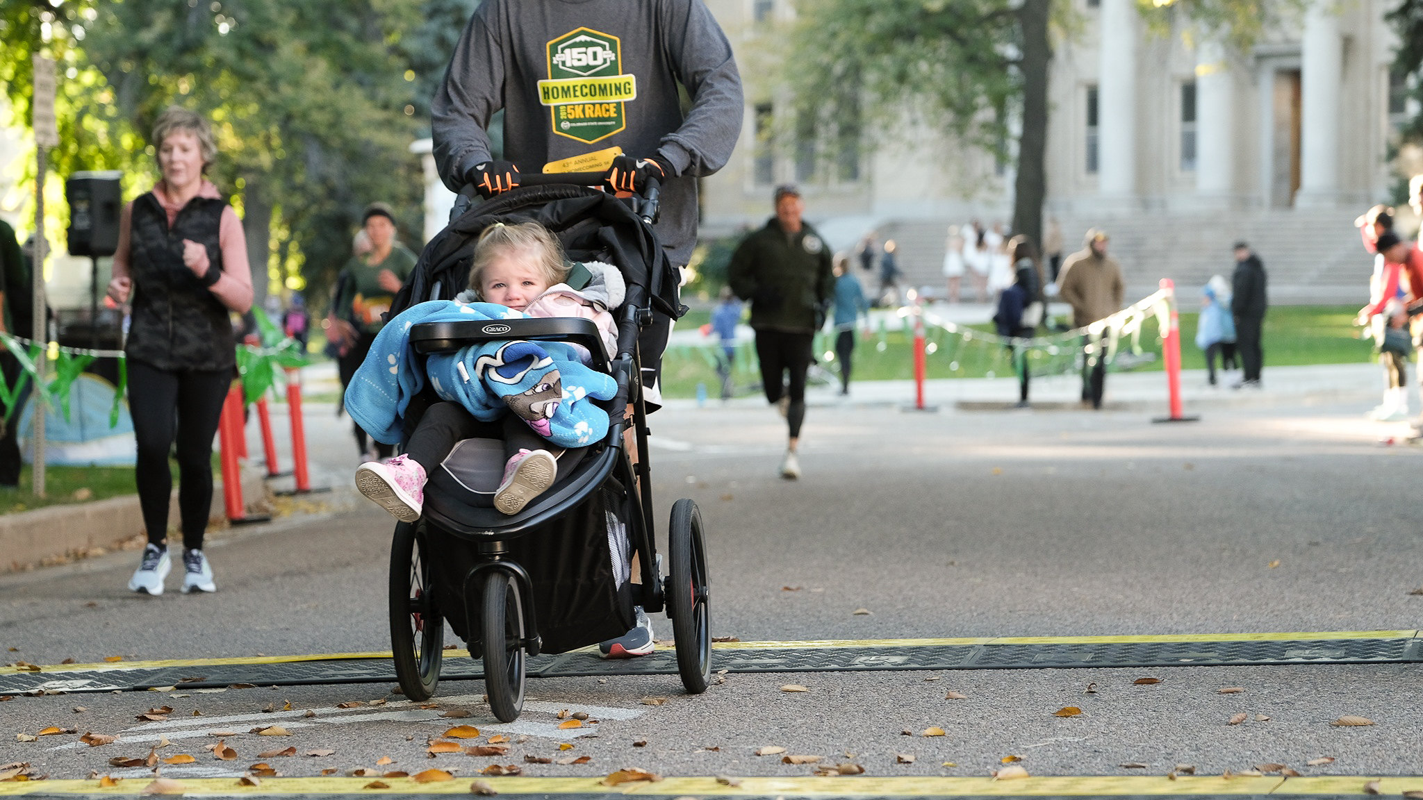 A little girl smiles from a stroller as she is pushed over the finish line