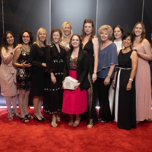 A group of women in front of a black background, on a red carpet.