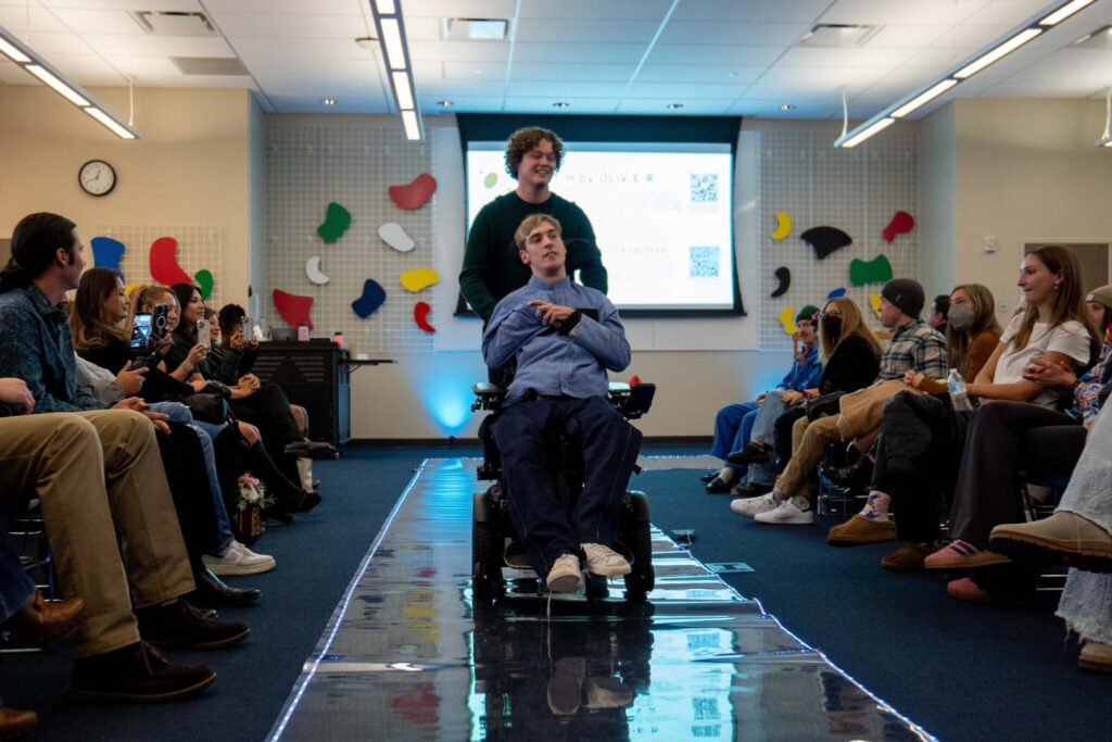 James moves down the runway in his wheelchair showcasing a pant and shirt set created by product development students with fit adjustments for those seated.